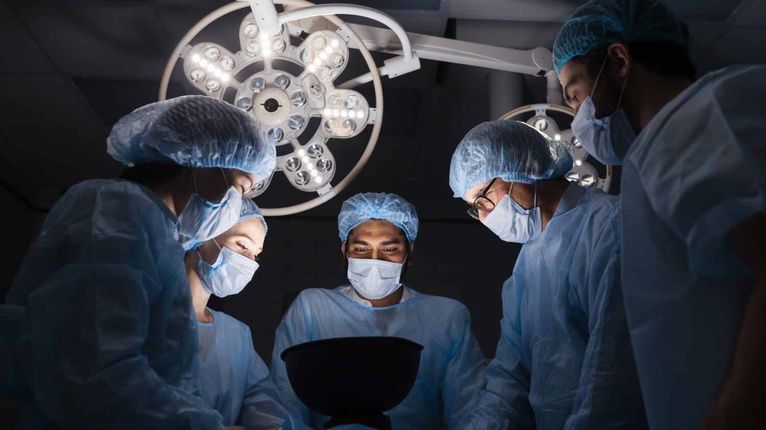 Low angle view of team of professional surgeons working at the hospital performing surgical procedure in operating theatre. Hospital, medicine, people, professional surgery equipment concept